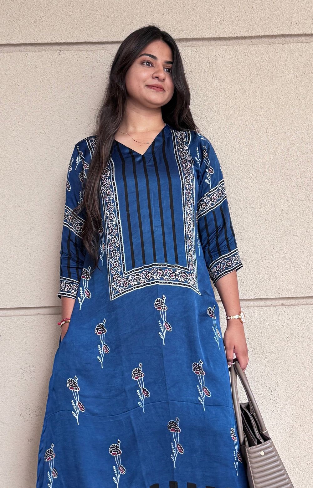 Woman wearing a blue embroidered kurta with black pants against a light gray wall.